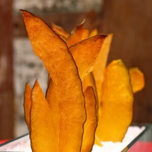 Vertical shot of crispy mango chips elegantly arranged in a clear container with a background blur.