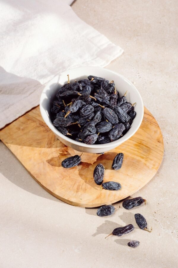 Still life of sun-dried raisins in a ceramic bowl on a wooden board, natural light.
